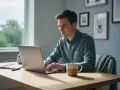 Mężczyzna pracuje na laptopie, przygotowując się do studiów magisterskich online. Na biurku notatnik i kubek kawy.