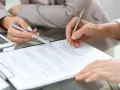 Dwie osoby podpisują dokumenty, co może być częścią ich praktyk zawodowych.