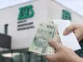 Ręce trzymają polskie banknoty przed budynkiem ZUS. To symboliczny moment, kiedy wypłata 14 emerytury staje się rzeczywistością.