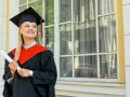Uśmiechnięta absolwentka z dyplomem, w todze i birecie, zastanawia się, co to studia MBA i jakie możliwości otwierają.