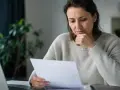 Zmartwiona kobieta czyta pismo, które informuje, że zabrano jej świadczenie pielęgnacyjne.