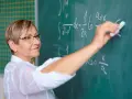 Nauczyciel początkujący pisze kredą wzory matematyczne na tablicy.
