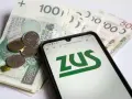 Na ekranie telefonu widnieje logo ZUS. Obok leżą polskie banknoty i monety. To może być druk z15 związany z finansami.