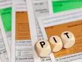 Drewniane klocki z literami "PIT" leżą na formularzach podatkowych. Temat: kwota wolna od podatku 2026.