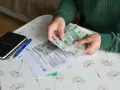 Ręce liczą banknoty 100 zł nad dokumentami ZUS. Obok leży kalkulator i długopis. To może być pomocne przy ustalaniu, ile wynosi świadczenie przedemerytalne na rękę.