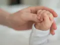 Dłoń rodzica obejmuje maleńką dłoń dziecka. To symbol miłości i wsparcia, jak świadczenie rodzicielskie.