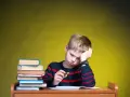 Chłopiec z podpartą głową siedzi przy biurku ze stosem książek i zeszytem.