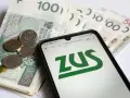 Złotówki i monety na tle ekranu telefonu z logo ZUS. To może być obrazek o okresowa emerytura kapitałowa.