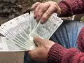 Ręce trzymające banknoty 100 zł. Czy to wystarczy na emeryturę po 30 latach pracy przy najniższej krajowej?