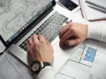 Architekt pracuje nad projektem na laptopie, analizując plany. Zastanawiasz się, ile zarabia architekt?