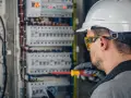 Elektryk w kasku i okularach ochronnych pracuje przy rozdzielnicy. Zastanawiasz się, ile zarabia elektryk?