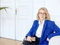 Kobieta w okularach i niebieskiej marynarce trzyma notatnik. Planuje dofinansowanie na otwarcie firmy.
