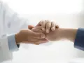 Lekarz w białym kitlu trzyma dłoń pacjenta, okazując wsparcie. To symbol troski i nadziei, ważny dla osób z niepełnosprawnością.