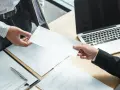 Przekazanie dokumentów, być może umowa na czas określony, między dłońmi nad biurkiem z laptopem.