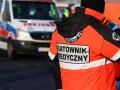 Ratownik medyczny w pomarańczowej kurtce z napisem "RATOWNIK MEDYCZNY" obok karetki. Zastanawiasz się, ile zarabia ratownik medyczny?