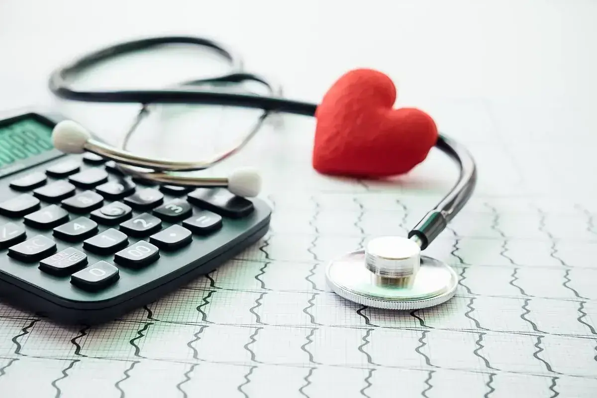 Stetoskop, kalkulator i czerwone serce na tle EKG symbolizują troskę o zdrowie i planowanie finansowe, w tym dobrowolne ubezpieczenie chorobowe.