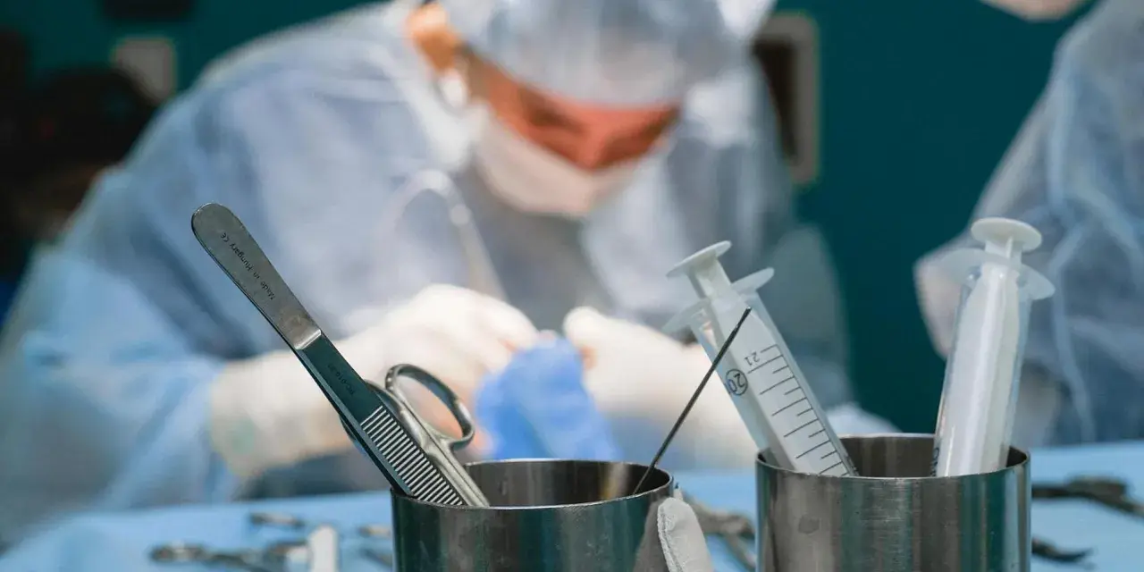 Chirurgowie w akcji. Zastanawiasz się, ile zarabia lekarz? W tle widać zespół medyczny podczas operacji, a na pierwszym planie narzędzia chirurgiczne i strzykawki.