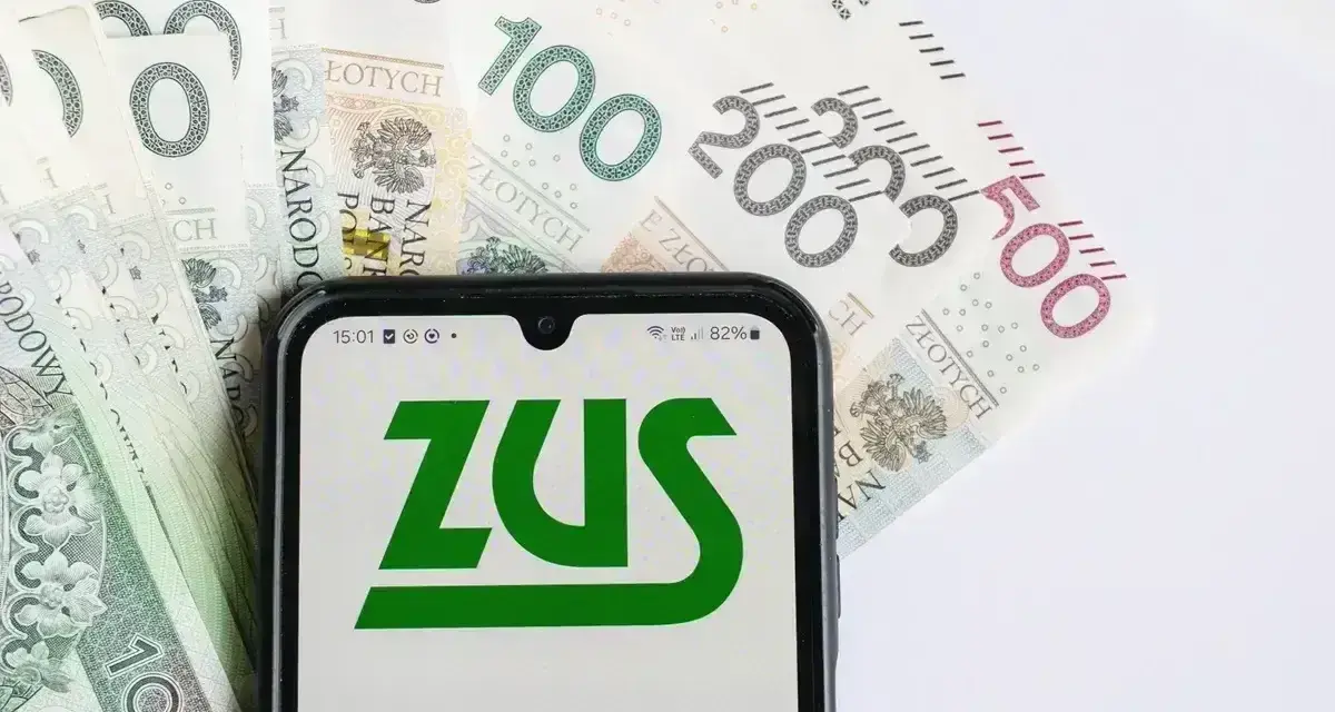 ZUS na ekranie telefonu, obok banknoty 100, 200 i 500 zł. Symbolizuje to zasiłek pogrzebowy 6000 zł.