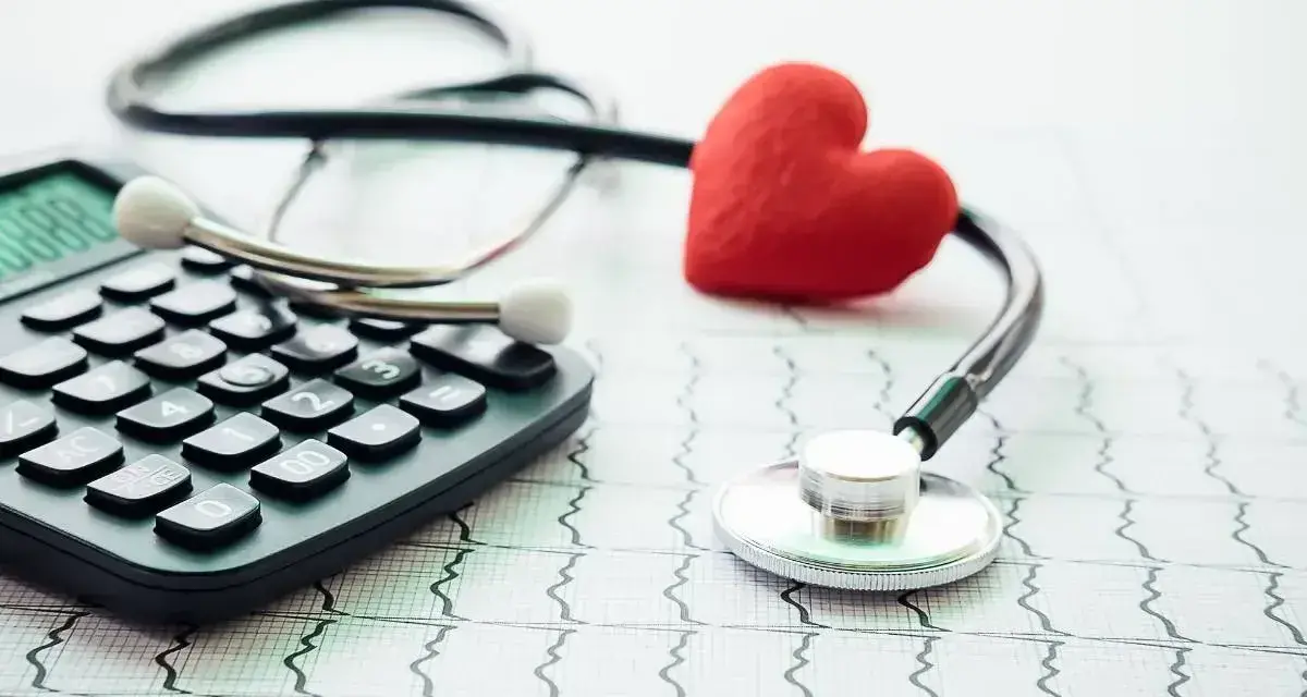 Stetoskop, kalkulator i czerwone serce na tle EKG symbolizują troskę o zdrowie i planowanie finansowe, w tym dobrowolne ubezpieczenie chorobowe.
