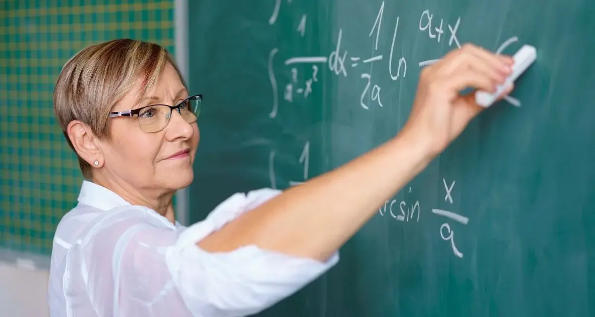 Nauczyciel początkujący pisze kredą wzory matematyczne na tablicy.