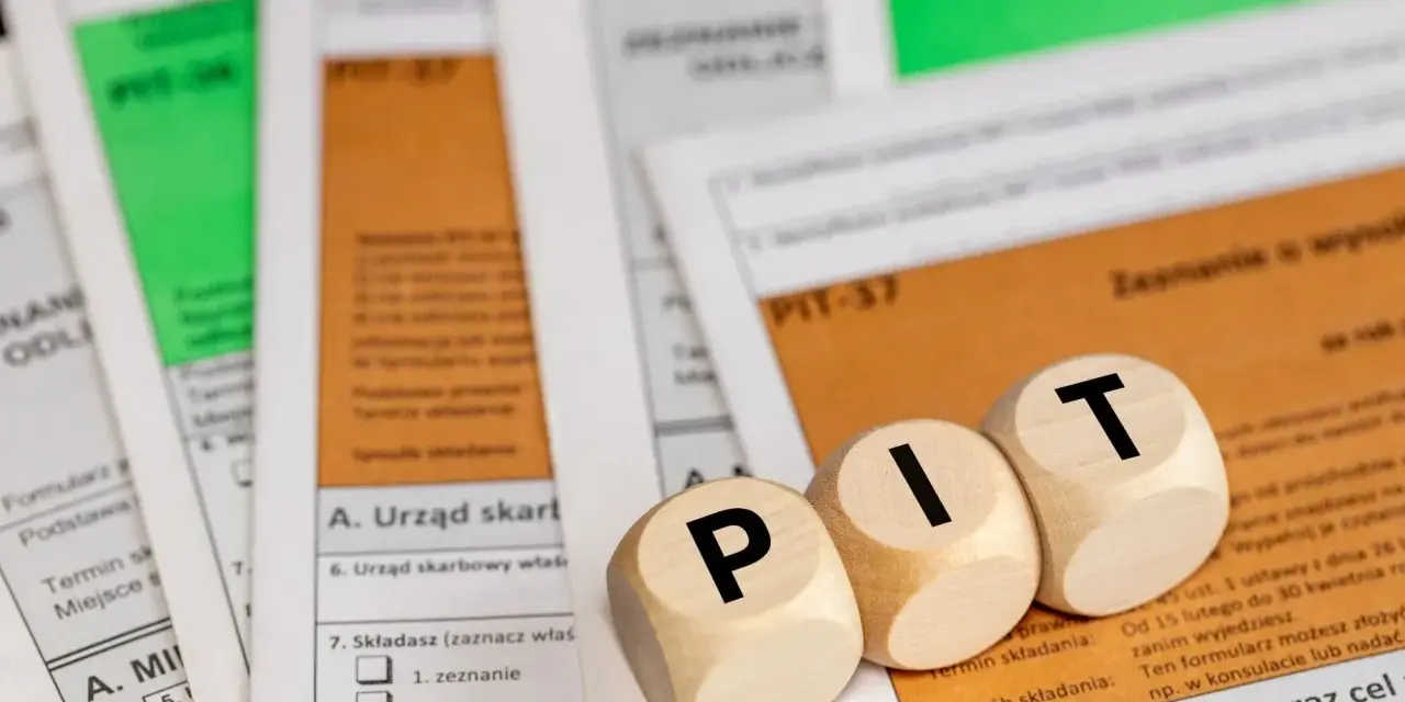 Drewniane klocki z literami "PIT" leżą na formularzach podatkowych. Temat: kwota wolna od podatku 2026.