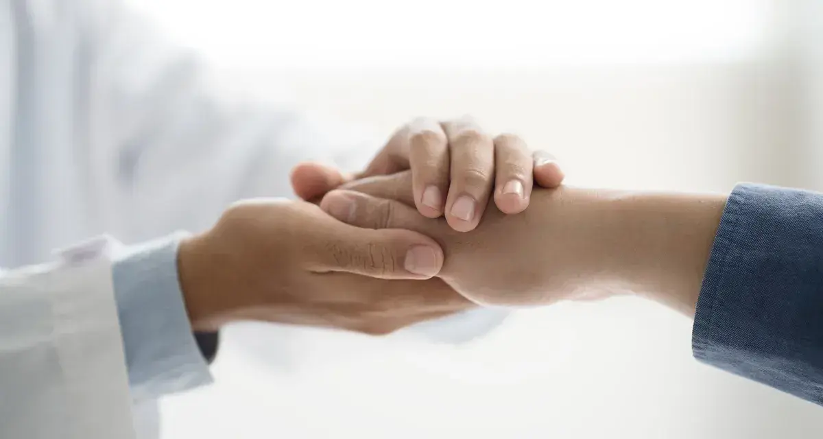 Lekarz w białym kitlu trzyma dłoń pacjenta, okazując wsparcie. To symbol troski i nadziei, ważny dla osób z niepełnosprawnością.