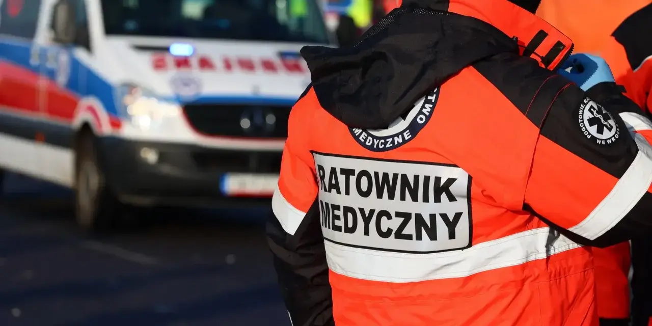 Ratownik medyczny w pomarańczowej kurtce z napisem "RATOWNIK MEDYCZNY" obok karetki. Zastanawiasz się, ile zarabia ratownik medyczny?