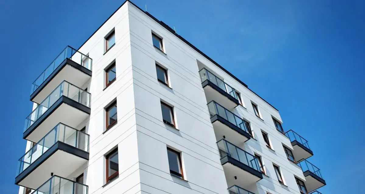 Nowoczesny budynek mieszkalny z balkonami i szklanymi balustradami, na tle błękitnego nieba. Idealne miejsce do życia, jak w pit 39.