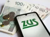 Na ekranie telefonu widnieje logo ZUS. Obok leżą polskie banknoty i monety. To może być druk z15 związany z finansami.