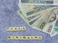 Płaca minimalna w Polsce – polskie banknoty o nominałach 100 i 500 zł ułożone na szarym tle, obok kafelki z literami tworzące napis "PŁACA MINIMALNA".