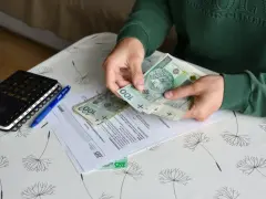 Ręce liczą banknoty 100 zł nad dokumentami ZUS. Obok leży kalkulator i długopis. To może być pomocne przy ustalaniu, ile wynosi świadczenie przedemerytalne na rękę.