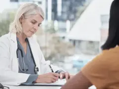 Lekarka w białym kitlu pisze receptę, być może kod C na L4, dla pacjentki.