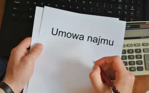 Ręka pisze długopisem na umowie najmu, obok kalkulator i laptop. Czas pomyśleć o podatku od najmu.