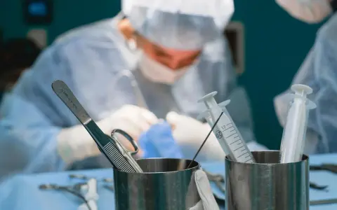 Chirurgowie w akcji. Zastanawiasz się, ile zarabia lekarz? W tle widać zespół medyczny podczas operacji, a na pierwszym planie narzędzia chirurgiczne i strzykawki.