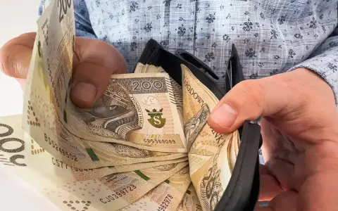 Ręce trzymają portfel z banknotami 200 zł. Czy to zapowiedź trzynastki w 2026 roku?