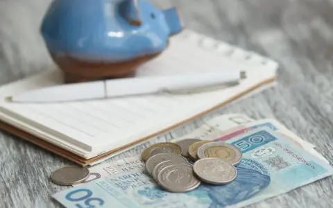 Świnka skarbonka, notatnik i długopis nad polskimi banknotami i monetami. Zastanawiasz się, ile wyniesie waloryzacja kapitału początkowego w 2025?
