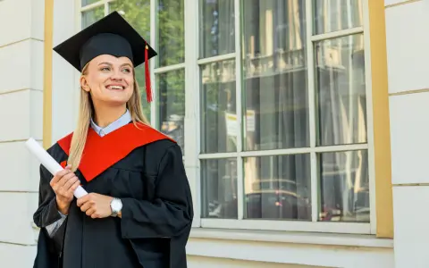 Uśmiechnięta absolwentka z dyplomem, w todze i birecie, zastanawia się, co to studia MBA i jakie możliwości otwierają.