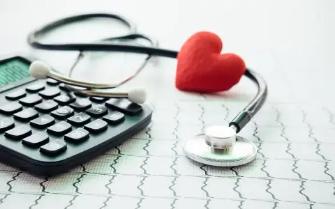 Stetoskop, kalkulator i czerwone serce na tle EKG symbolizują troskę o zdrowie i planowanie finansowe, w tym dobrowolne ubezpieczenie chorobowe.