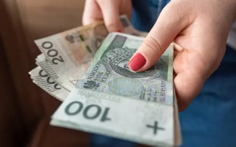 Dłoń trzyma stos polskich banknotów 100 i 200 zł. Pieniądze mogą być przeznaczone na przelew podatkowy.
