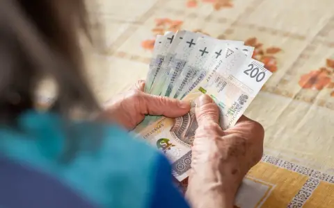 Dłonie starszej osoby liczą banknoty 200 zł. Tabela 14. emerytury może zawierać takie kwoty.