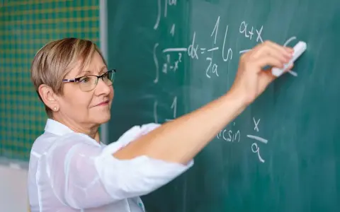Nauczyciel początkujący pisze kredą wzory matematyczne na tablicy.