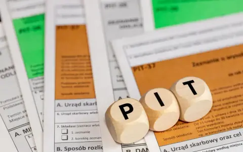 Drewniane klocki z literami "PIT" leżą na formularzach podatkowych. Temat: kwota wolna od podatku 2026.