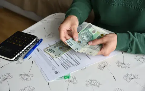 Ręce liczą banknoty 100 zł nad dokumentami ZUS. Obok leży kalkulator i długopis. To może być pomocne przy ustalaniu, ile wynosi świadczenie przedemerytalne na rękę.