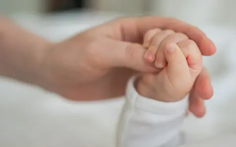 Dłoń rodzica obejmuje maleńką dłoń dziecka. To symbol miłości i wsparcia, jak świadczenie rodzicielskie.