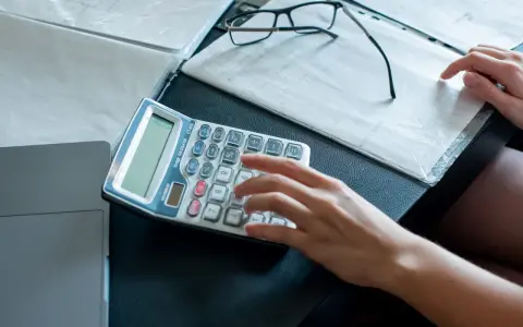 Ręce liczą na kalkulatorze dokumenty, analizując umowę zlecenie i potencjalne problemy z komornikiem.