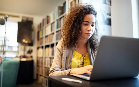 Kobieta z kręconymi włosami uczy się, jak sprawdzić swój NIP, korzystając z laptopa w bibliotece.