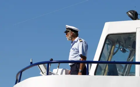 Kapitan na mostku statku, w białym mundurze i czapce, spogląda w dal. Zastanawiasz się, ile zarabia marynarz?