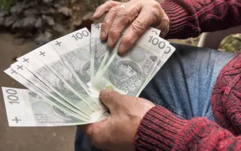 Ręce trzymające banknoty 100 zł. Czy to wystarczy na emeryturę po 30 latach pracy przy najniższej krajowej?