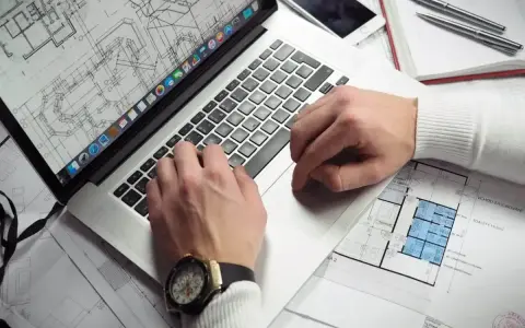 Architekt pracuje nad projektem na laptopie, analizując plany. Zastanawiasz się, ile zarabia architekt?