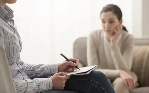 Psycholog notuje, analizując sytuację pacjentki. Zarobki psychologa zależą od doświadczenia i specjalizacji.